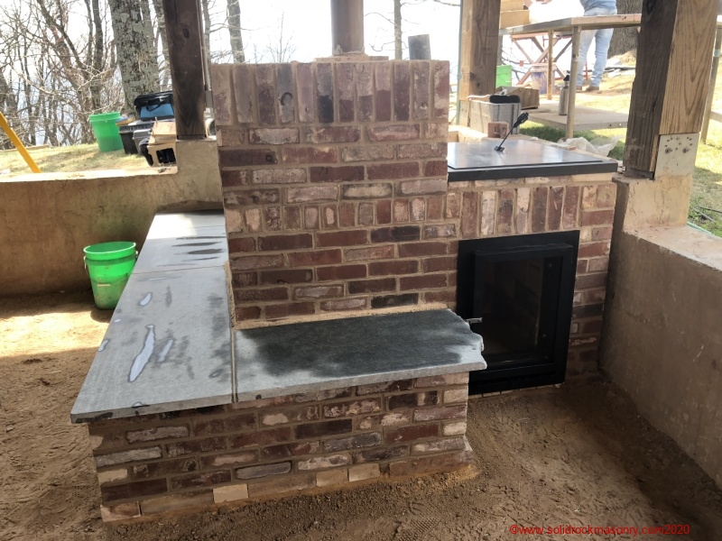 Small-masonry-heater-with-3-sided-heated-bench-finished-in-brick.-Built-at-a-workshop-in-Little-Switzerland-NC