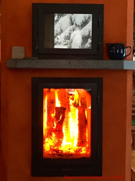 Fire burning in masonry heater with snow reflection on oven glass