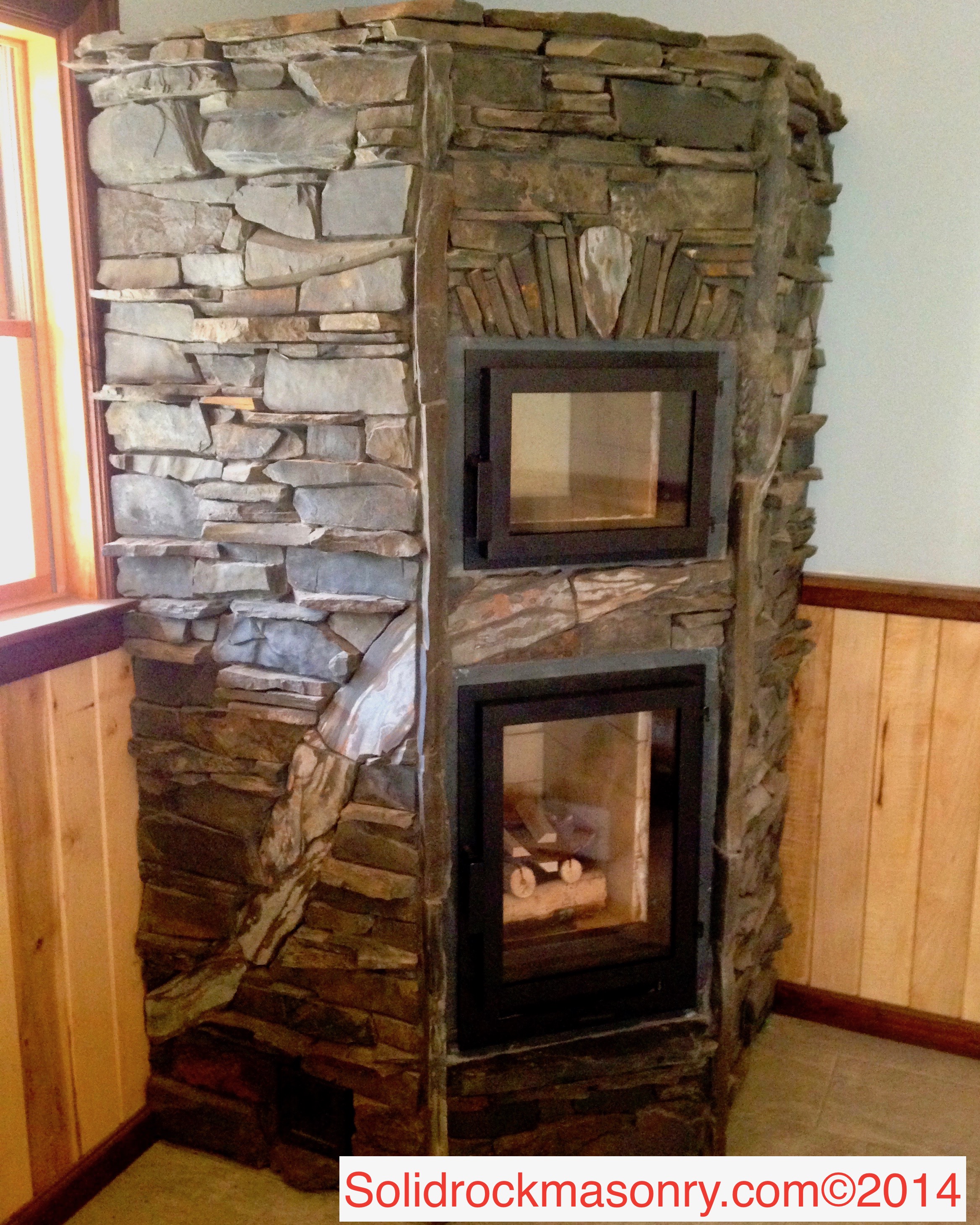 Rogotzke SR-13 corner masonry heater with white oven and heated bench.  Finished with Slate and a band of taconite stone tile.