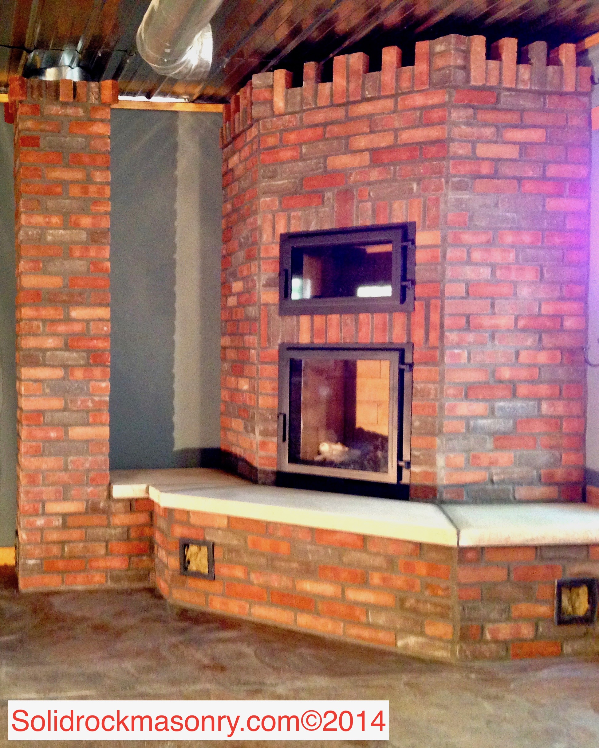 Fearing SR-18 Corner Masonry Heater unit with black oven, hot water loop, & heated bench. Finished in brick and limestone hearth.